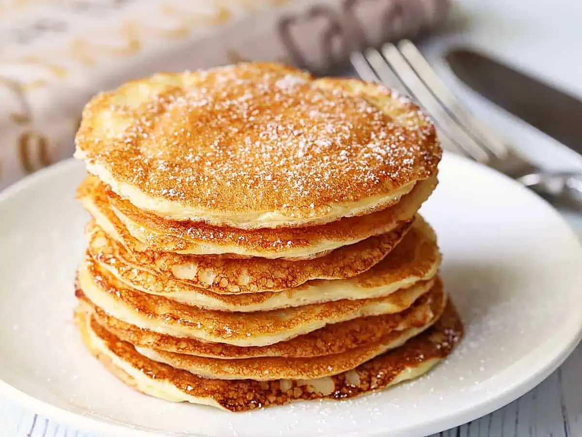 Ein Stapel goldbrauner Protein Pancakes, best&auml;ubt mit Puderzucker. Perfekt f&uuml;r ein gesundes Fr&uuml;hst&uuml;ck oder als leckeres proteinreiches Dessert.