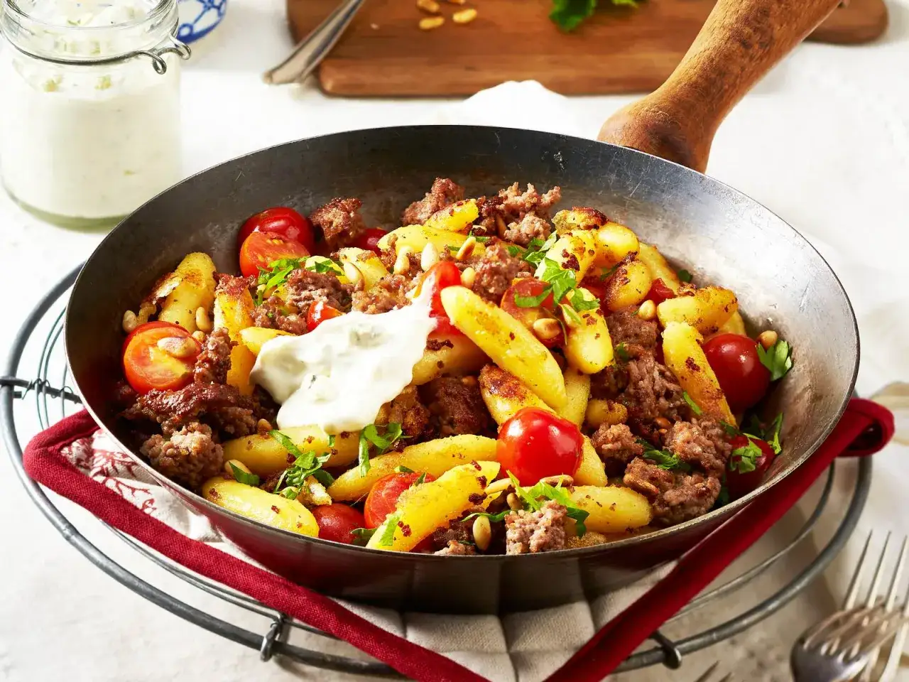 Schupfnudeln mit Hackfleisch, Kirschtomaten und Pinienkernen in einer Pfanne, garniert mit einem Klecks Dip.