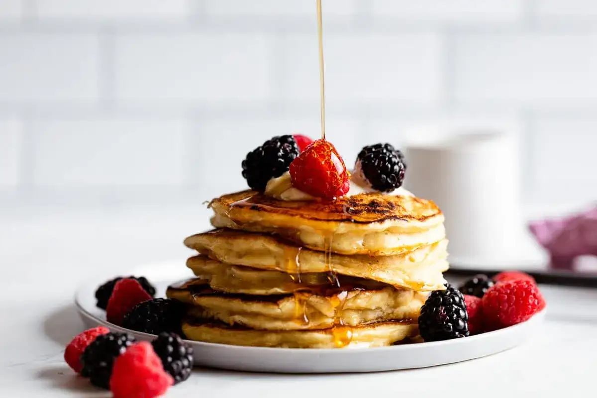 Ein Stapel amerikanischer Pancakes mit Beeren und Sirup, der darauf gegossen wird.