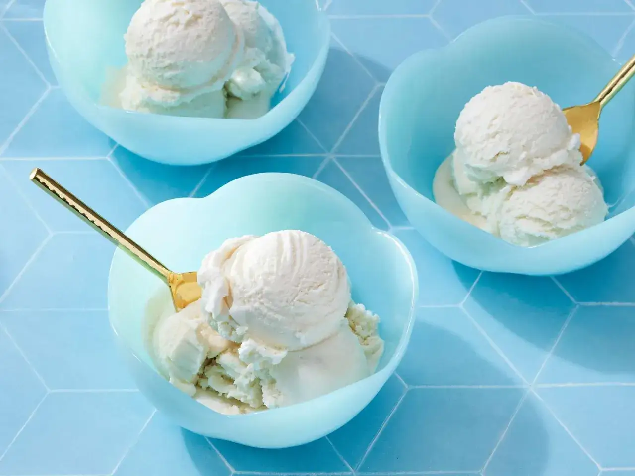 Drei Schalen mit cremigem Vanilleeis, perfekt zum Vanilleeis selber machen. Goldene L&ouml;ffel warten darauf, das k&ouml;stliche Dessert zu genie&szlig;en.