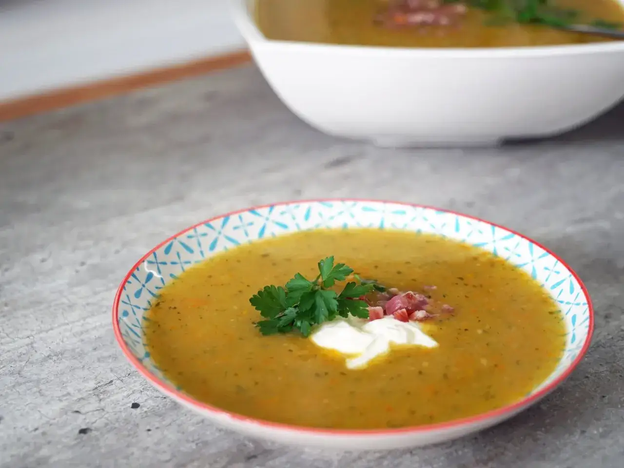 Eine cremige Kartoffelsuppe, zubereitet im Thermomix, garniert mit einem Klecks Sahne, Petersilie und Speckw&uuml;rfeln.