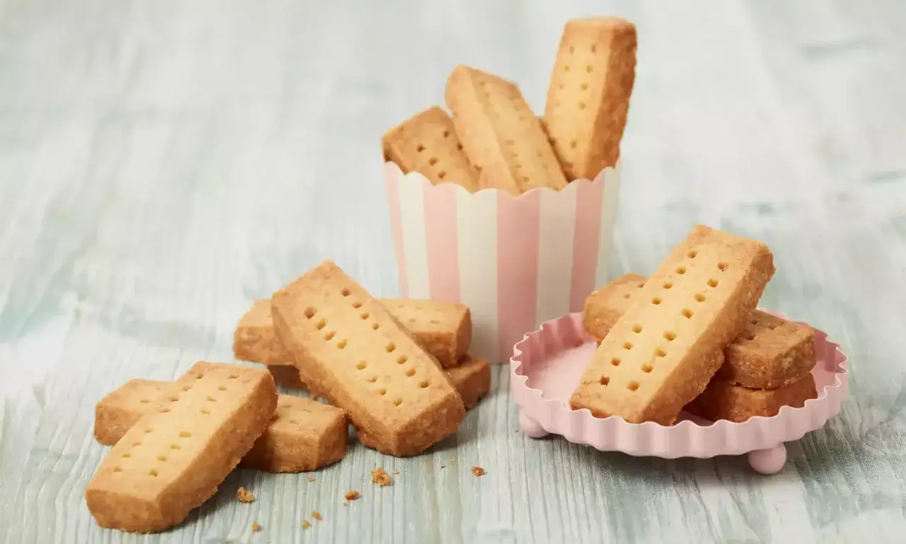 Goldbraune Shortbread-Riegel, perfekt für ein einfaches Shortbread Rezept, liegen auf einem rosa Teller und in einer gestreiften Schale.