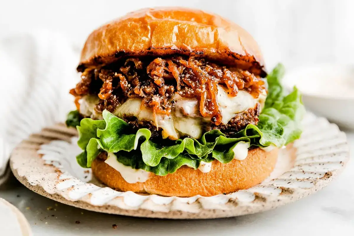 Saftiger Burger mit geschmolzenem K&auml;se, knackigem Salat und karamellisierten Portwein Zwiebeln auf einem rustikalen Teller.