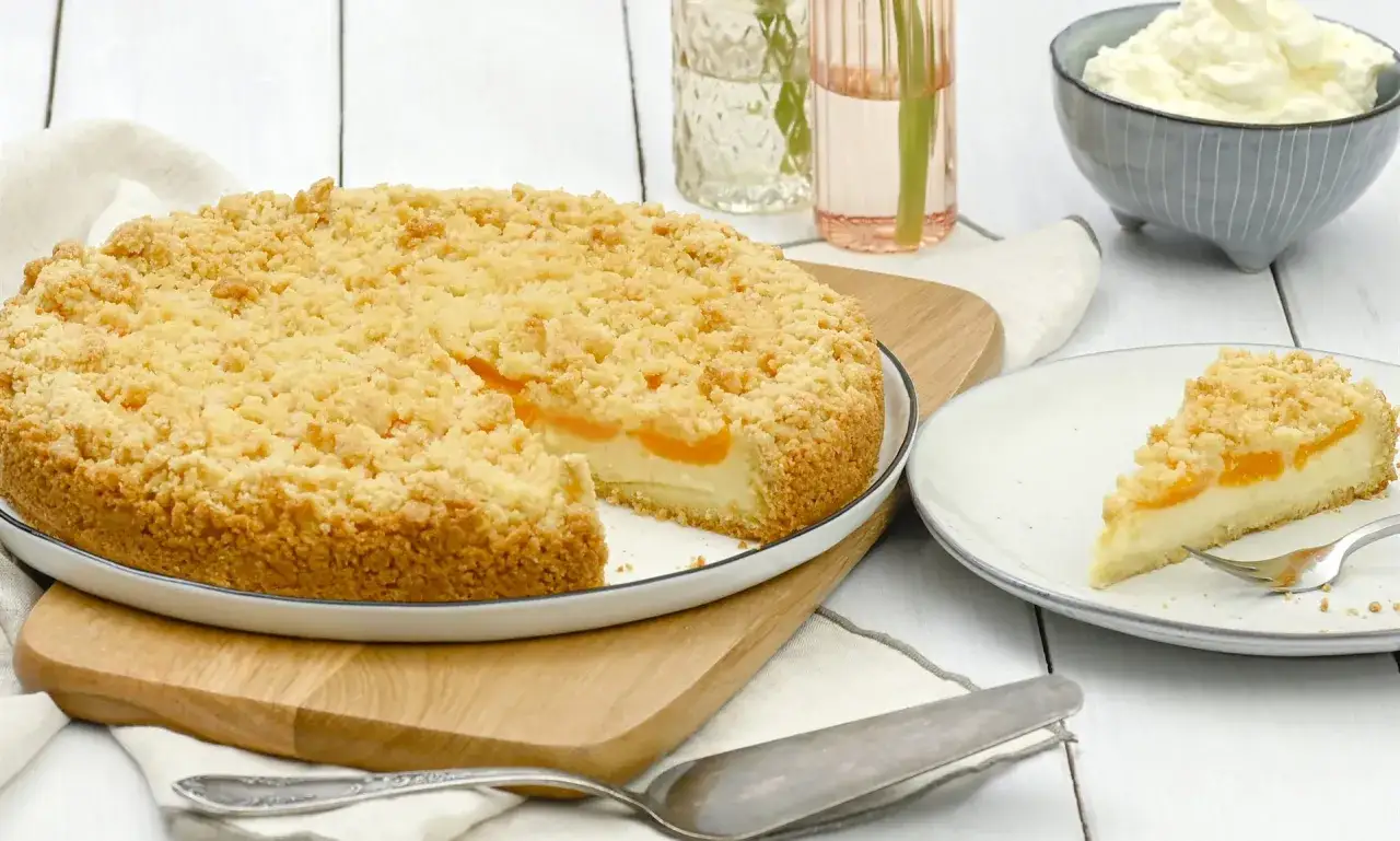 Ein saftiger Streuselkuchen mit Pudding und Fruchtf&uuml;llung, gebacken in einer Springform. Ein St&uuml;ck davon liegt auf einem Teller.