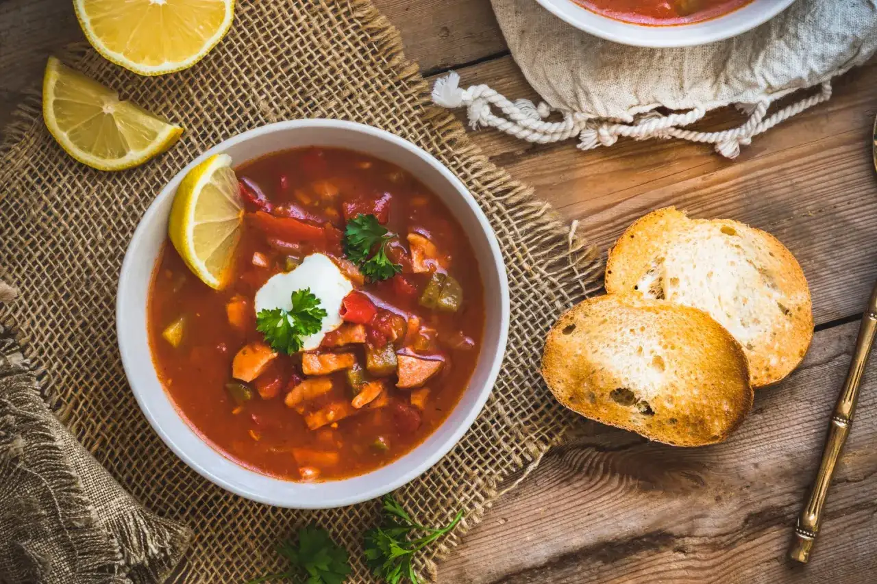 Herzhaftes Soljanka Rezept: Eine Sch&uuml;ssel voller w&uuml;rziger Suppe mit Fleisch, Gem&uuml;se, einem Klecks Sahne und Zitrone, serviert mit ger&ouml;stetem Brot.