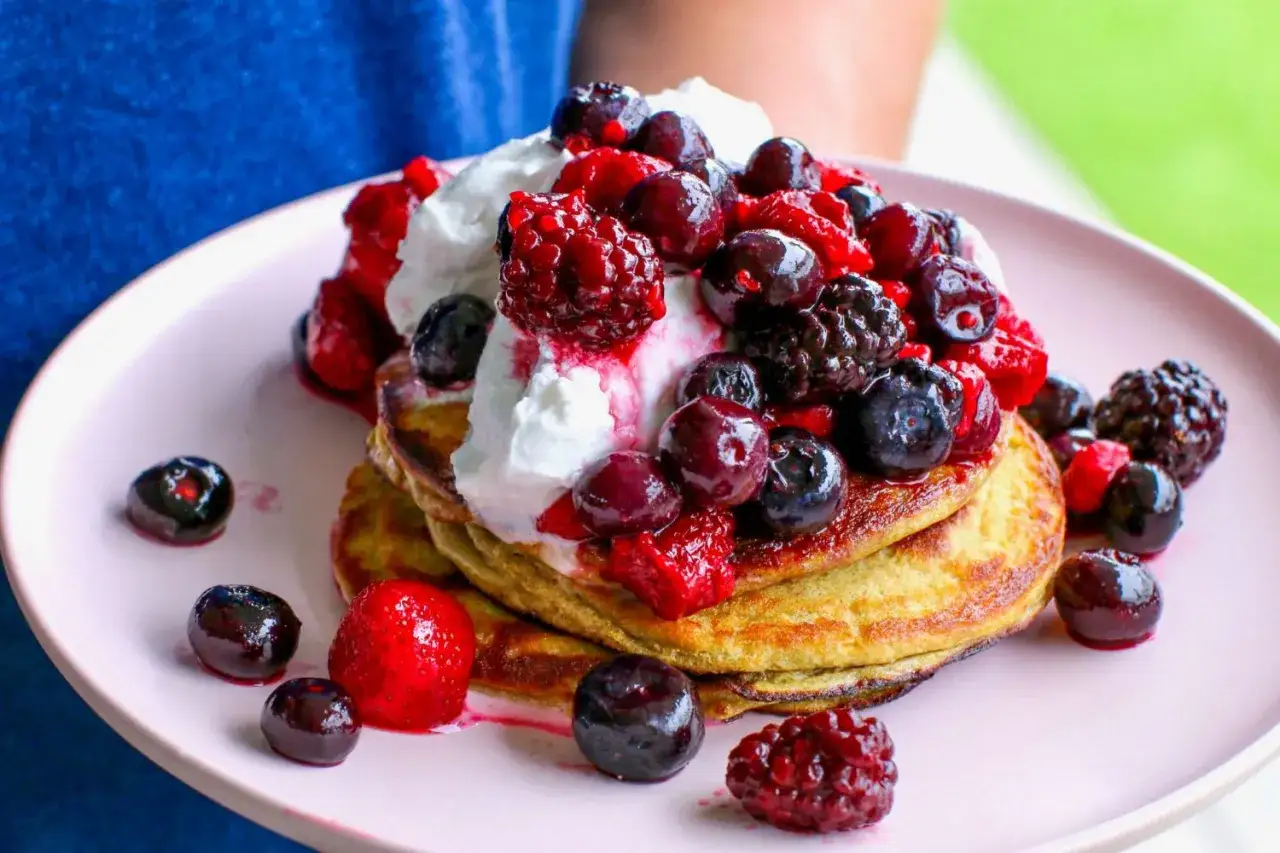 Ein Stapel protein Kaiserschmarrn mit Sahne und frischen Beeren wie Blaubeeren, Himbeeren und Erdbeeren.