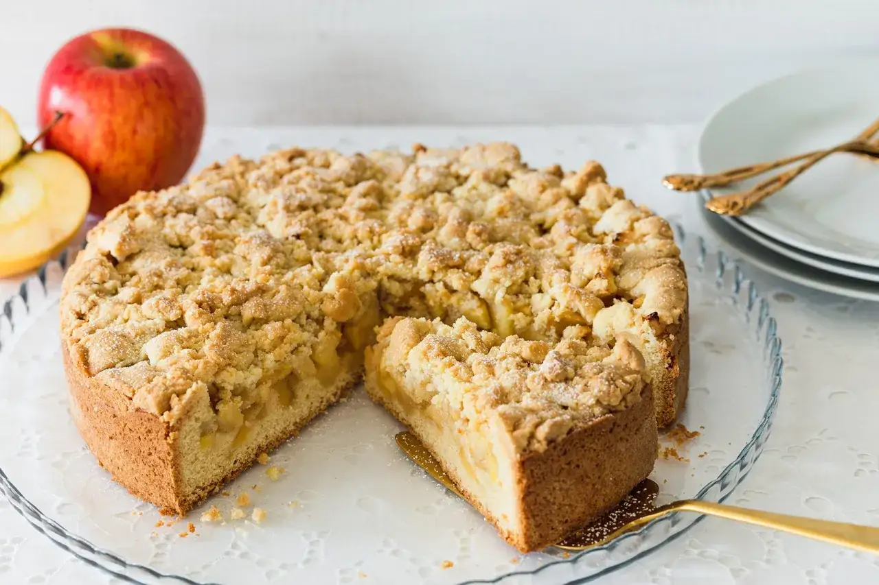 Ein saftiger omas apfelkuchen mit Streuseln, daneben &Auml;pfel. Ein St&uuml;ck ist bereits herausgeschnitten.