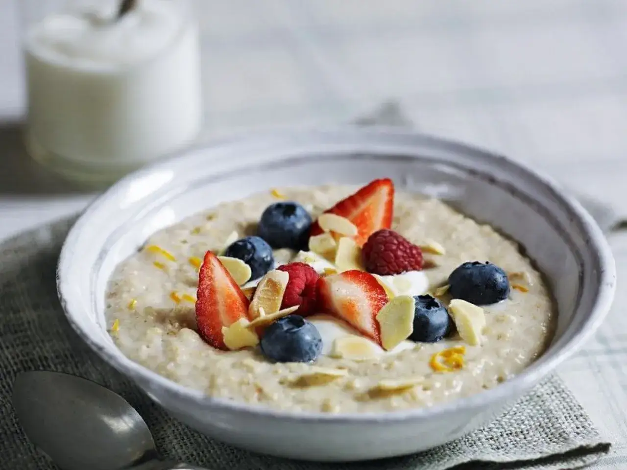 Schüssel mit cremigem Porridge, garniert mit frischen Beeren, Mandelsplittern und einem Klecks Joghurt. Ein gesundes Porridge Rezept für den Morgen.