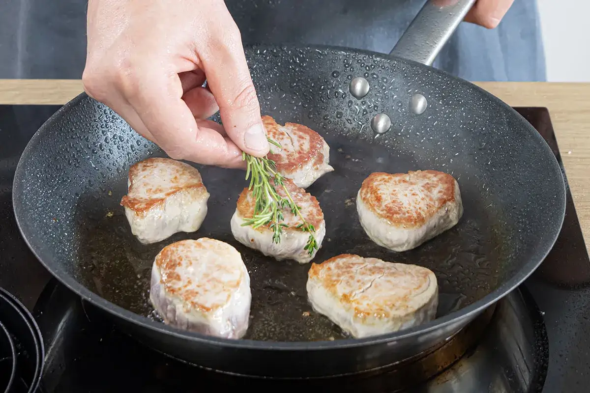 Zarte schweine medaillons braten in der Pfanne. Ein Rosmarinzweig wird hinzugefügt, um das Aroma zu verfeinern.