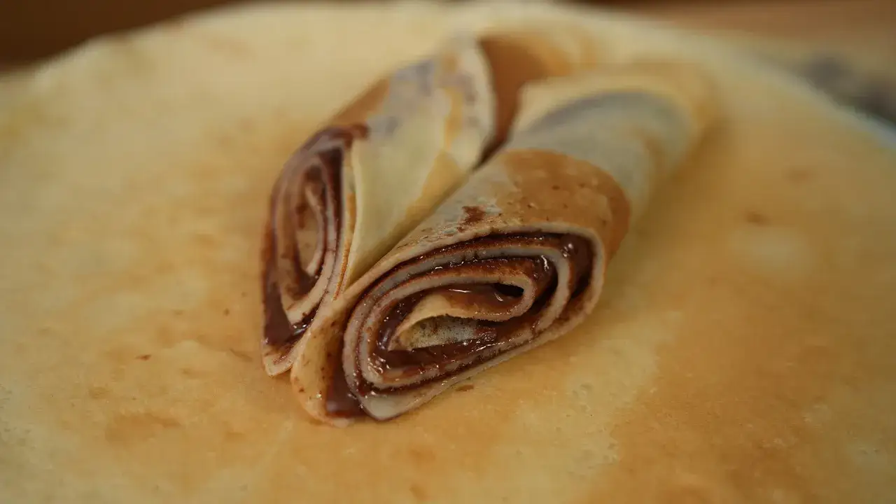 Zwei gerollte Pfannkuchen mit Schokoladencreme, die auf einem weiteren Pfannkuchen liegen. Der Pfannkuchenteig ist goldbraun gebacken.
