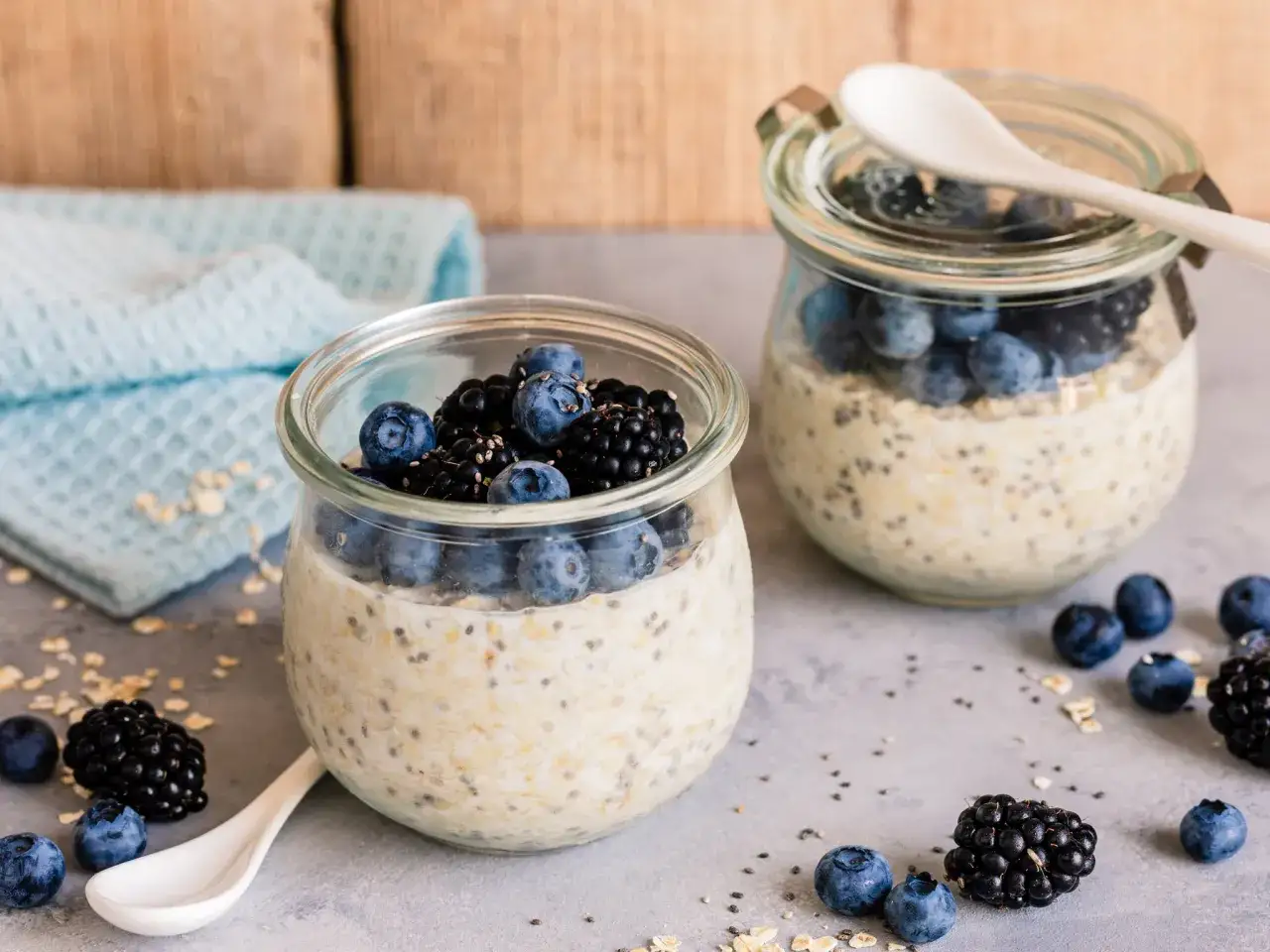 Zwei Gläser mit Overnight Oats, garniert mit Blaubeeren und Brombeeren. Perfekt für einen gesunden Start in den Tag.
