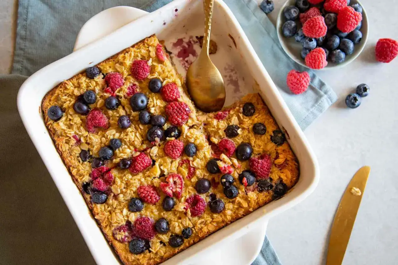 Leckeres baked oats rezept mit frischen Beeren in einer Auflaufform. Ein goldener L&ouml;ffel wartet darauf, probiert zu werden.