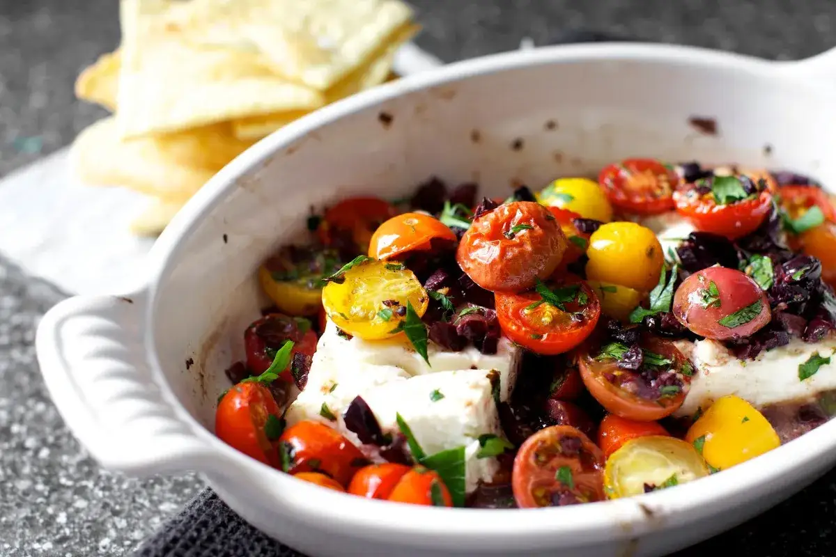 Ofenfrische Hauptgerichte mit Feta: Kirschtomaten und Oliven &uuml;berbacken mit cremigem Feta, serviert mit knusprigem Brot.