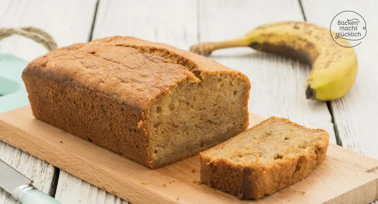 Saftiges Bananenbrot mit Dinkelmehl, eine Scheibe abgetrennt, daneben eine Banane. Backen macht glücklich!