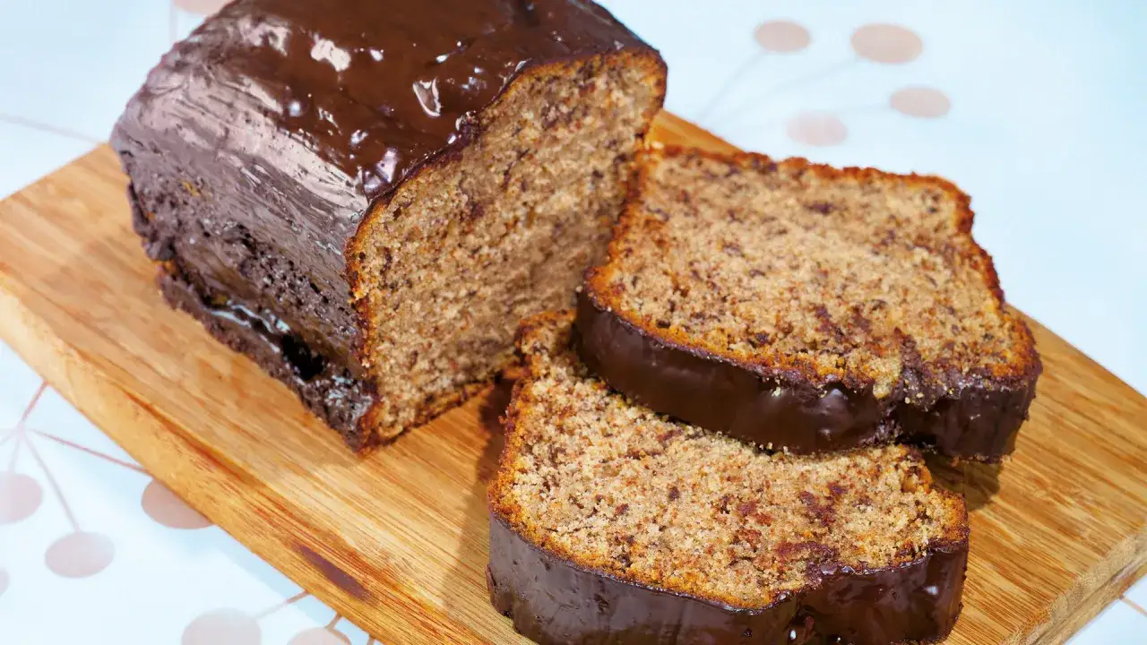 Ein saftiger schoko bananen kuchen mit glänzender Schokoladenglasur, auf einem Holzbrett angeschnitten.