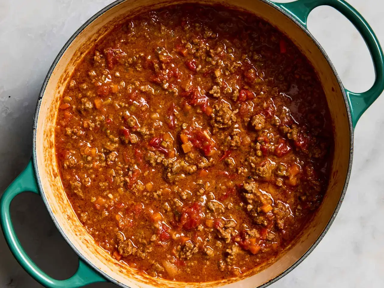 Herzhafte, schnelle Bolognese k&ouml;chelt in einem gr&uuml;nen Topf. Hackfleisch, Tomaten und Gem&uuml;se sind sichtbar.