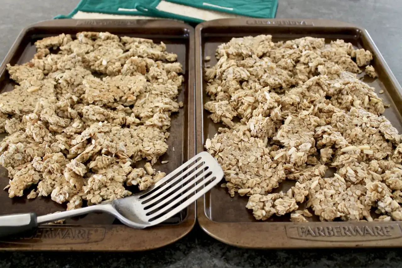 Zwei Backbleche voller selbstgemachtem Granola, bereit zum Backen. Eine Gabel liegt daneben.
