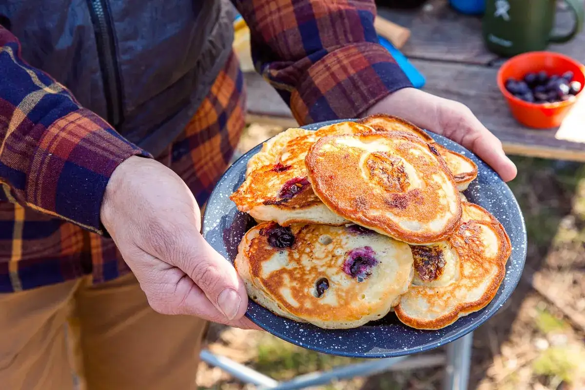 Goldbraune Bananenpfannkuchen mit Blaubeeren auf einem Teller, bereit zum Genie&szlig;en im Freien.