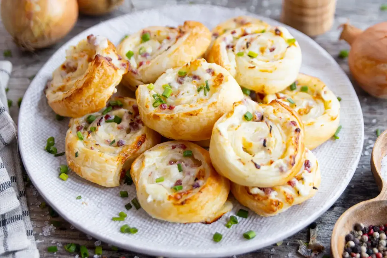 Leckere Flammkuchen Schnecken mit Speck und Zwiebeln, bestreut mit frischem Schnittlauch, auf einem Teller angerichtet.