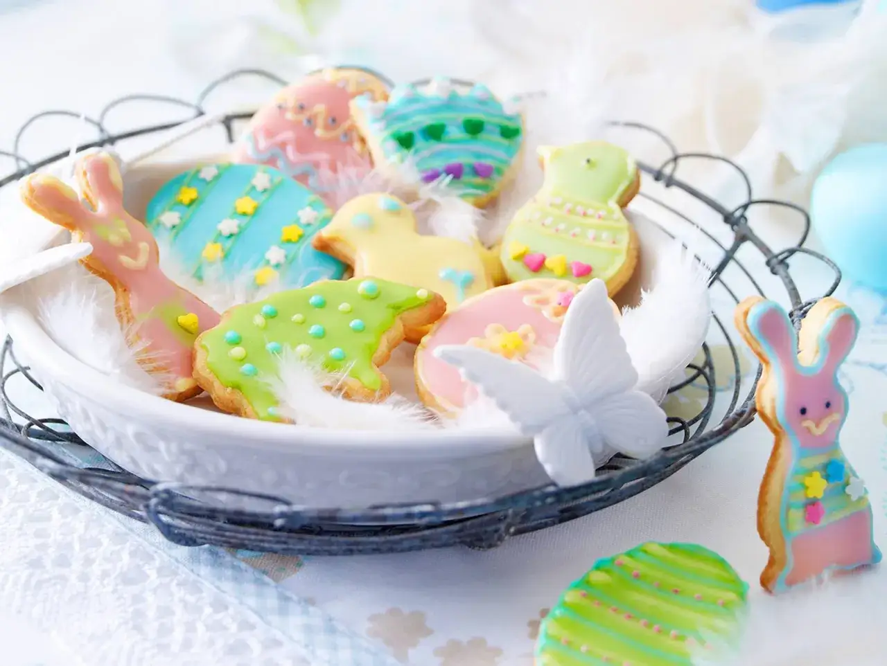 Bunte Osterkekse mit Zitronengeschmack, verziert als Hasen, Küken und Eier, liegen in einem Korb mit Federn.