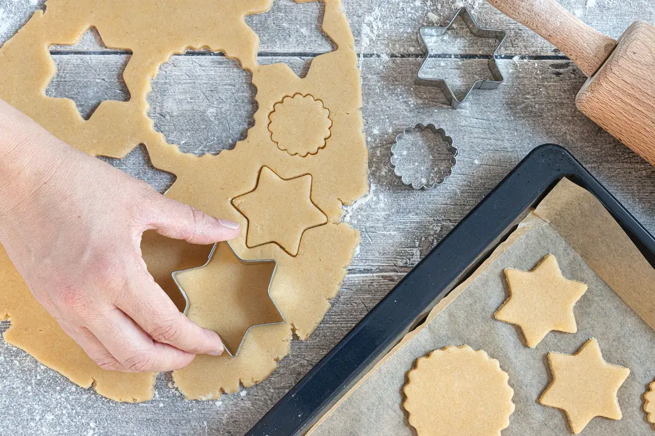 Hand formt Sterne aus Teig f&uuml;r Weihnachtskekse. Auf dem Blech liegen bereits fertige Sterne.