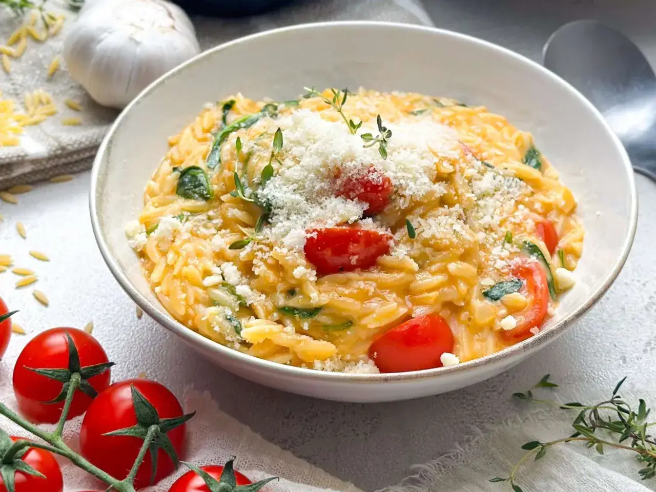 Cremige Orzo Nudeln mit Kirschtomaten, Spinat und Parmesan, garniert mit frischem Thymian. Ein köstliches Gericht, das Lust auf mehr macht.