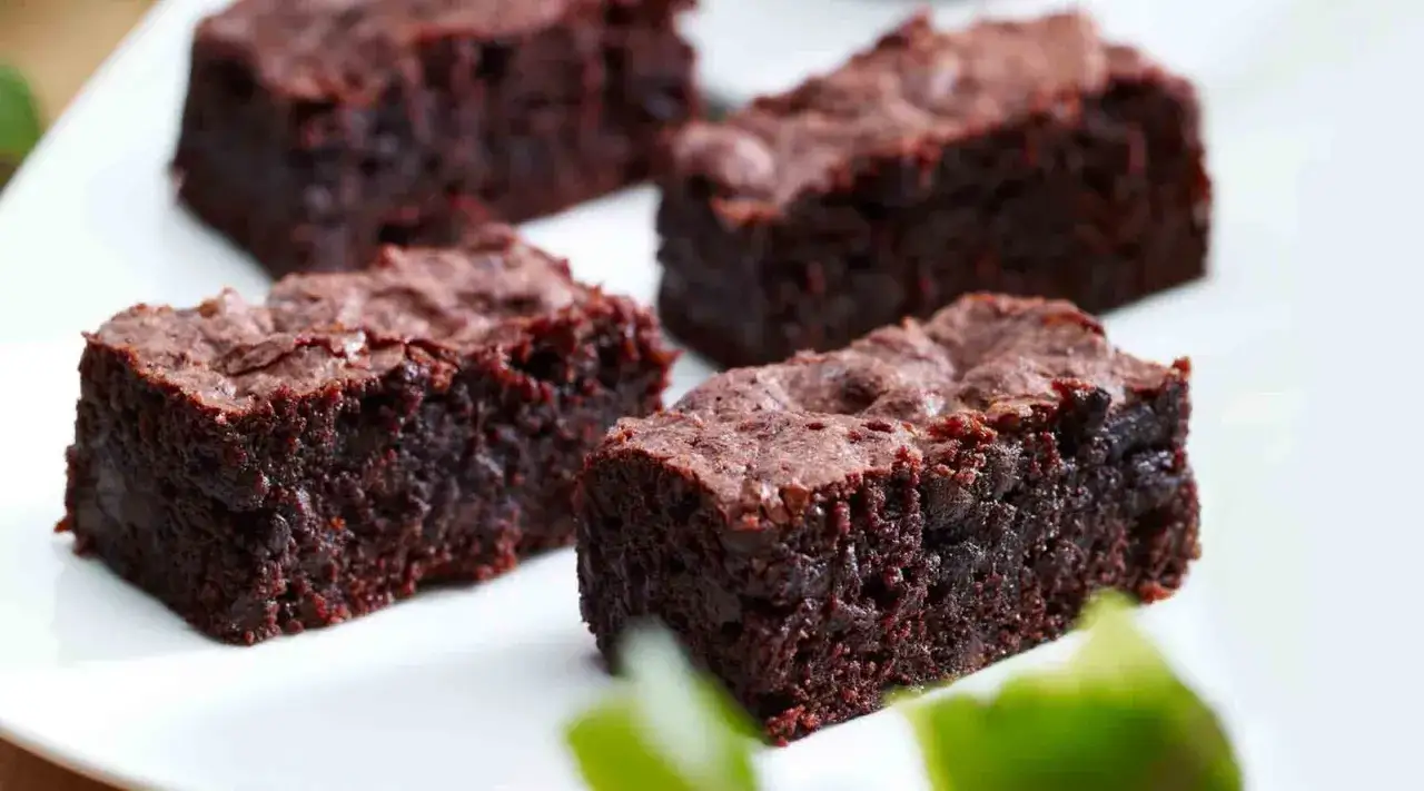 Saftige Brownies, perfekt für ein einfaches brownie rezept. Sie sind auf einem weißen Teller angerichtet, mit grünen Akzenten im Vordergrund.