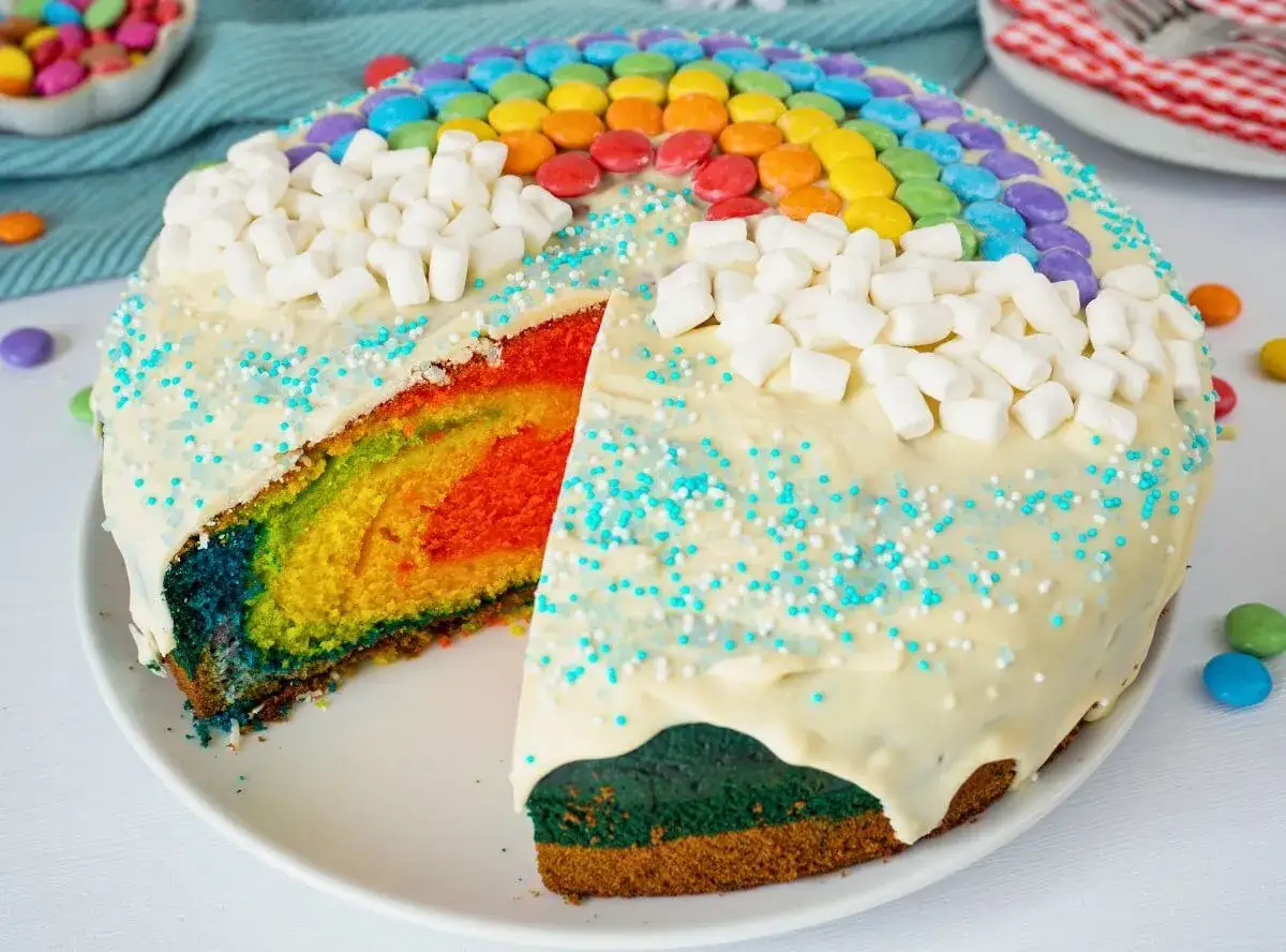 Ein bunter regenbogen kuchen mit Marshmallows und bunten Streuseln. Die bunten Schichten im Inneren sind ein echter Hingucker.