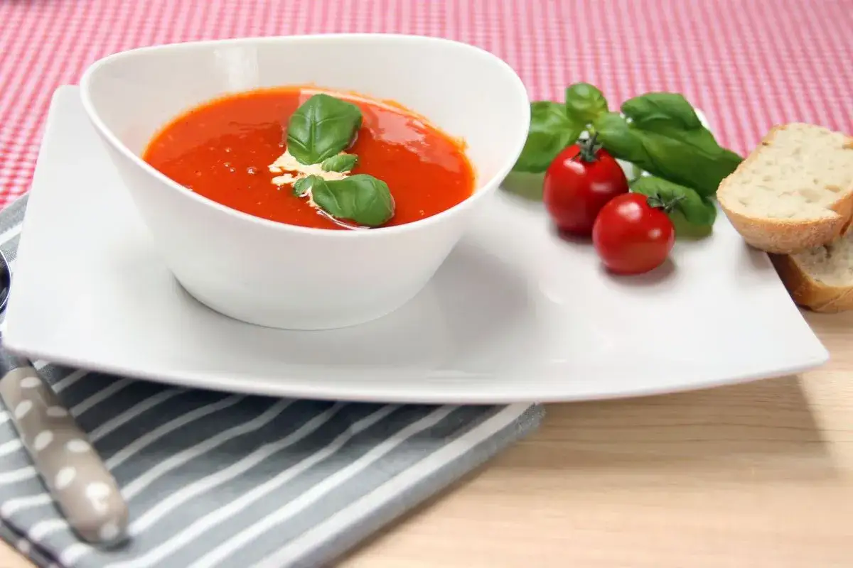 Eine cremige Tomatensuppe, zubereitet im Thermomix, garniert mit frischem Basilikum und einem Klecks Sahne. Dazu passen ger&ouml;stete Brotscheiben.