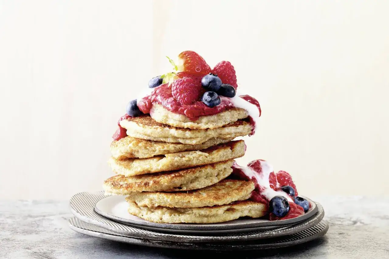 Ein Stapel goldbrauner Pancakes, garniert mit Joghurt, Beeren und Fruchtp&uuml;ree. Ein k&ouml;stliches Pancakes Rezept mit Joghurt f&uuml;r den perfekten Start in den Tag.