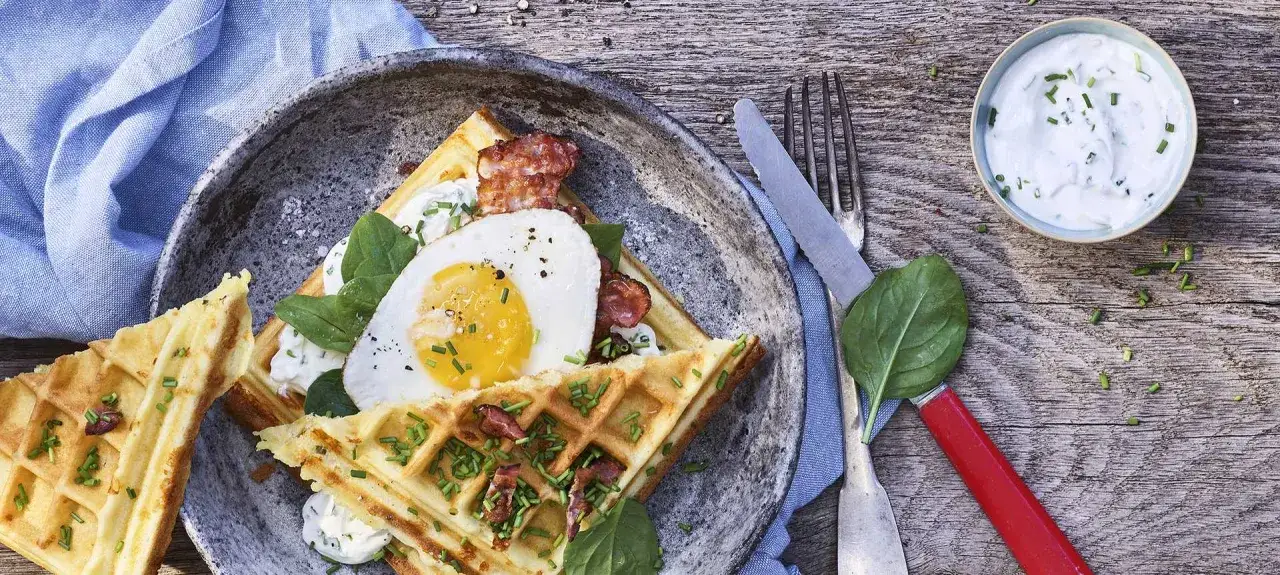 Herzhafte Waffeln mit Spiegelei, Speck und frischem Spinat, garniert mit Schnittlauch. Dazu ein Klecks Dip.