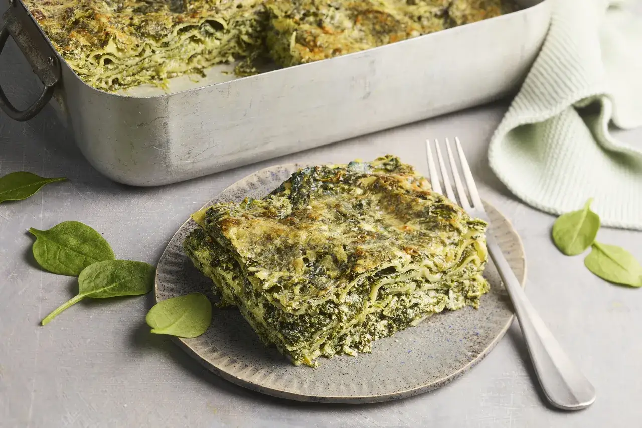 Herzhaftes Spinatlasagne Rezept: Eine Portion der cremigen Lasagne mit viel Spinat und Käse auf einem Teller, daneben frische Spinatblätter.