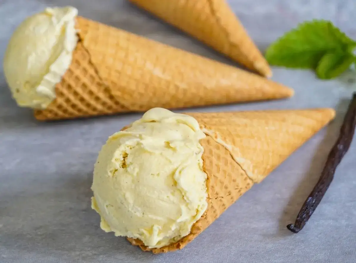 Vanilleeis in Waffelt&uuml;ten, frisch aus der Eismaschine. Daneben eine Vanilleschote und Minze.