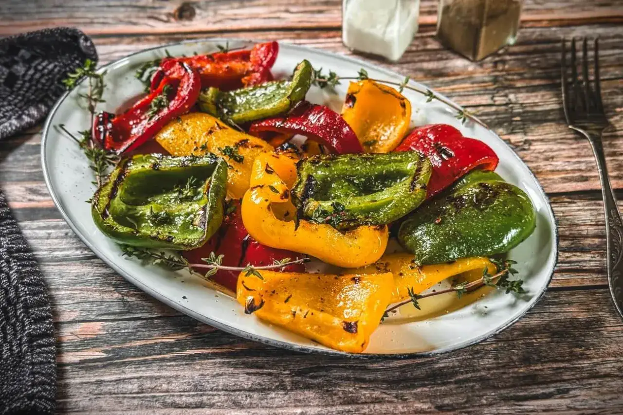Bunte, gegrillte Paprikast&uuml;cke mit Kr&auml;utern auf einem Teller. Perfekt zum Paprika grillen!