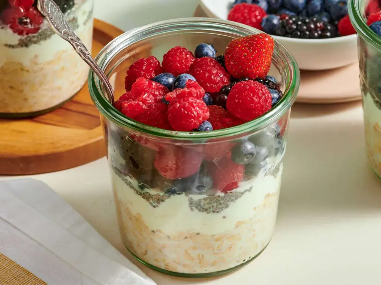 Ein Glas mit Overnight Oats, Joghurt und frischen Beeren wie Himbeeren, Blaubeeren und Erdbeeren.
