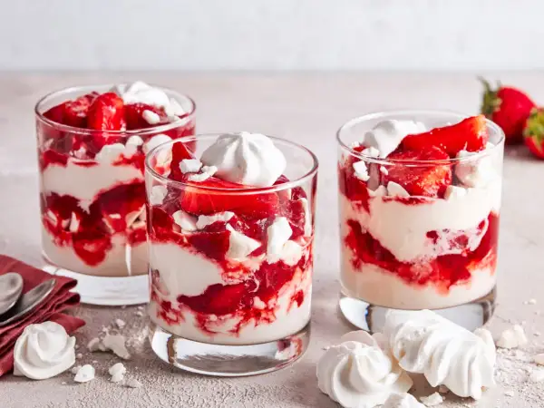 Drei Gläser mit Eton Mess: geschichtete Erdbeeren, Sahne und zerbrochene Baiser-Stücke. Ein süßer Genuss!