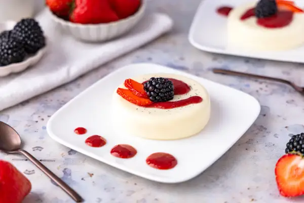 Cremige Panna Cotta, einfach im Thermomix zubereitet, garniert mit frischen Beeren und Erdbeersauce.