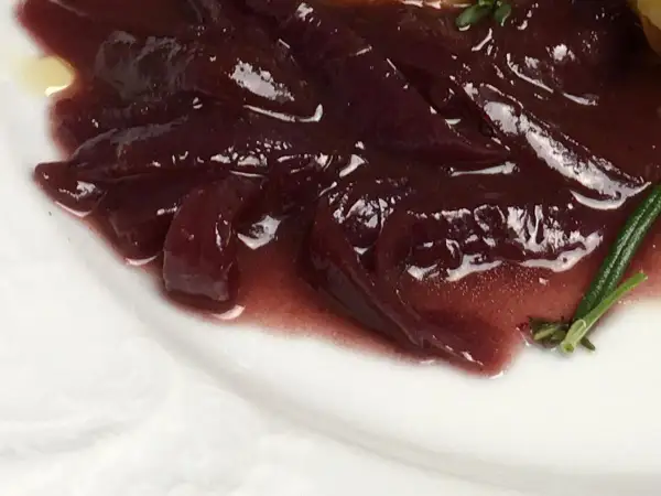 Portwein zwiebeln in einer glänzenden, dunklen Sauce auf einem weißen Teller, garniert mit Rosmarin.