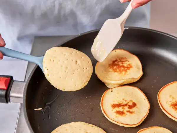 Pancakes rezept mit joghurt: goldbraune Pfannkuchen werden in einer Pfanne gebacken, ein Löffel Teig wird hinzugefügt.