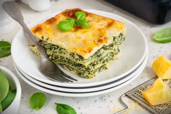 Ein Stück Spinatlasagne mit Käse überbacken, garniert mit Basilikum. Ein köstliches spinatlasagne rezept.