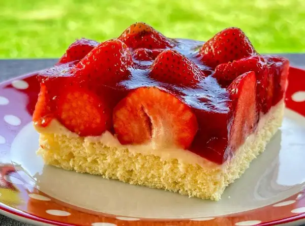 Ein Stück saftiger, **schneller Erdbeerkuchen vom Blech ohne Pudding**, belegt mit frischen Erdbeeren und glänzendem Tortenguss.