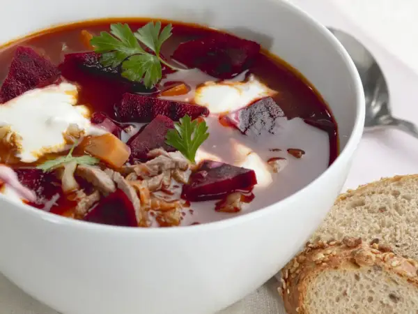 Herzhaftes Borschtsch-Rezept: Rote Bete, Fleisch und ein Klecks Sahne in einer Schüssel, dazu Brot.