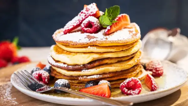 Ein Stapel amerikanischer Pancakes, bestäubt mit Puderzucker und garniert mit frischen Beeren und Minze.