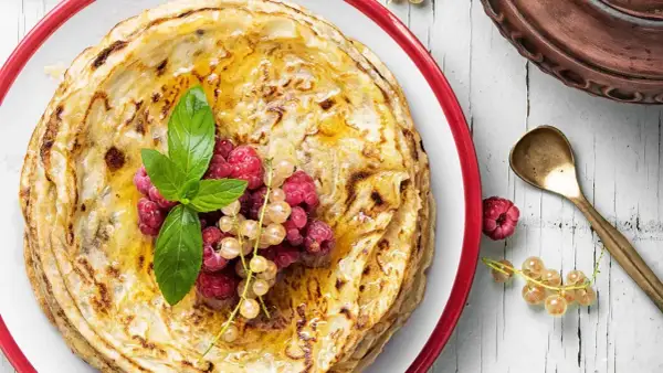 Gestapelte Pfannkuchen ohne Mehl, beträufelt mit Honig und garniert mit frischen Beeren und Minze. Ein köstlicher Genuss!