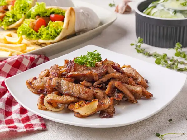 Saftiges Fleisch für ein köstliches Gyros Rezept, garniert mit Petersilie. Daneben liegen Gyros-Wraps und ein Gurkensalat.