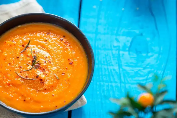 Eine cremige Tomatensuppe, zubereitet im Thermomix, garniert mit Rosmarin und Chiliflocken, serviert auf einem blauen Holztisch.