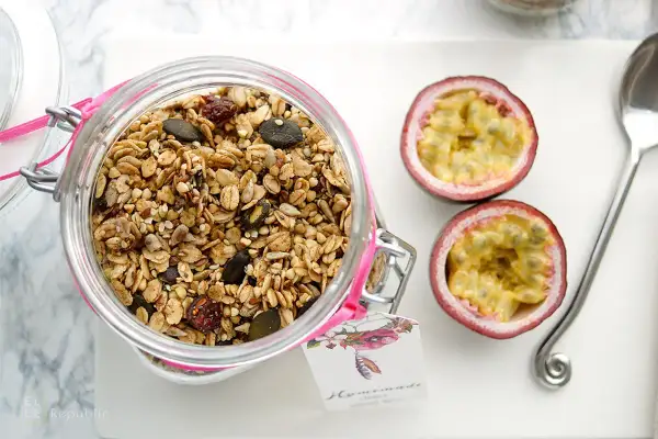 Glas mit selbstgemachtem Granola, Kürbiskernen und Trockenfrüchten. Daneben zwei Passionsfrüchte und ein Löffel.