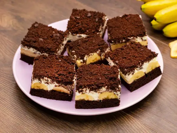 Saftiger Maulwurfkuchen vom Blech mit Bananen und Schokostreuseln auf einem rosa Teller.