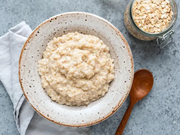 Cremiger Haferbrei in einer Schale, daneben ein Glas Haferflocken. Ein einfaches Porridge Rezept für einen gesunden Start.