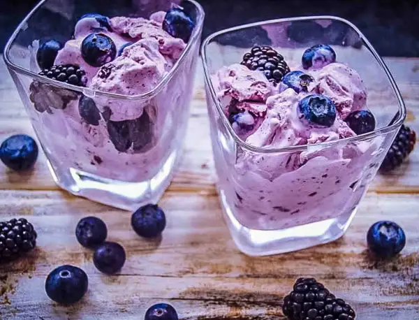Zwei Gläser mit cremigem, lila gefärbtem frozen joghurt, garniert mit frischen Blaubeeren und Brombeeren.